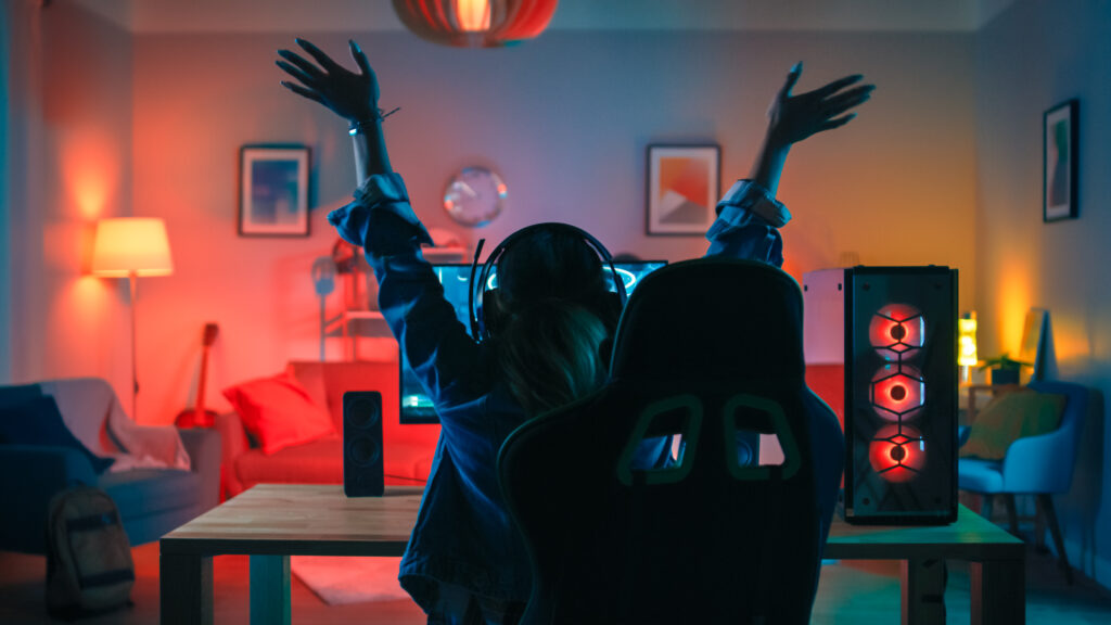 Back Shot of a Gamer Girl Playing and Winning on her on Her Powerful Personal Computer. Room and PC have Colorful Neon Led Lights.