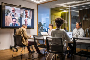 A group of business people hold a meeting with both in-person and virtual attendance.