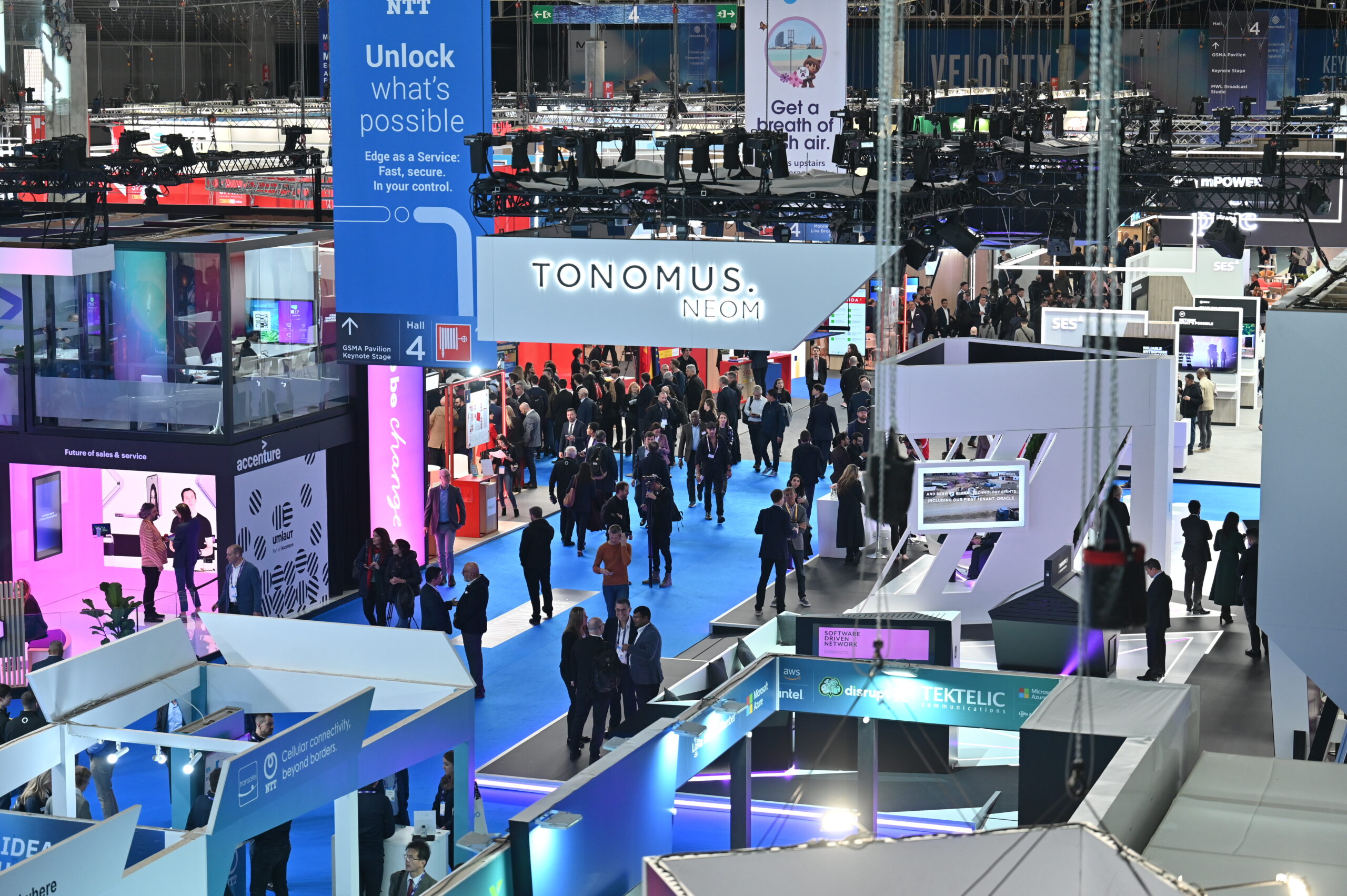 A busy technology convention show floor, illuminated with blue lights